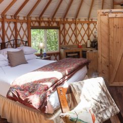 One full sized bed with white sheets and red blankets inside a Pacific Yurt.