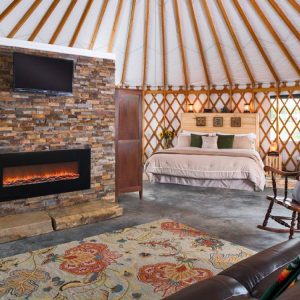 A yurt living room with a rocking chair and leather couch surrounding a gas fireplace.