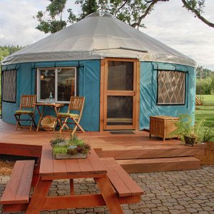 Yurt with a wooden wrap around porch and a picnic table on a stone patio.